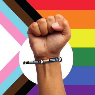 Pride Bracelet around someone's wrist, with an LGBTIQ+ flag in the background. Pride Bracelet around someone's wrist, with an LGBTIQ+ flag in the background.
