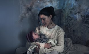 Woman holding baby in a room with moldy walls