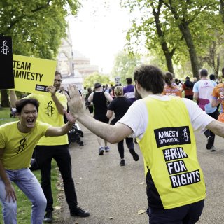 Amnesty Runner highfives a supporter with sign of team Amnesty in the background and many people running a marathon