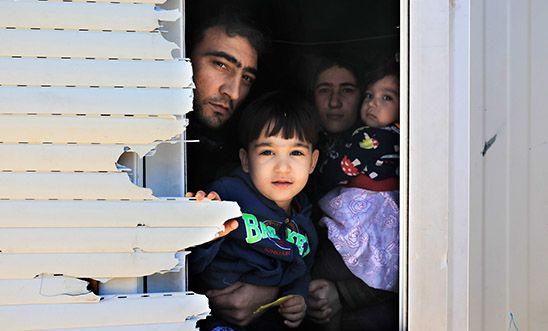 A family peeks through the window of the shipping container that is their temporary home