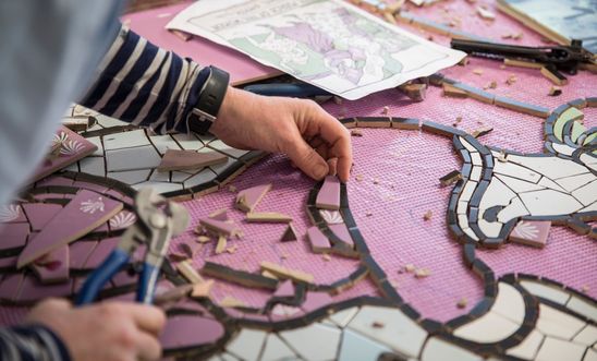 The artist's hand places ceramic pieces in a mural 