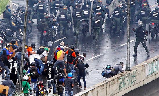 A member of the riot security forces points a gun towards a crowd of demonstrators in Venezuela