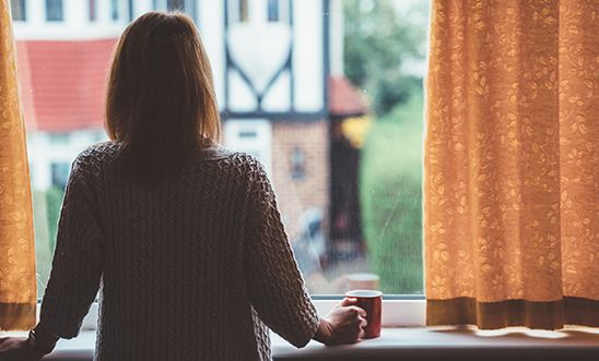 Rear view of woman at home staring through the window