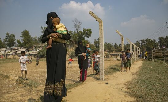 Rohingya refugees walk near a fence that is being constructed around the refugee camp on December 11, 2019