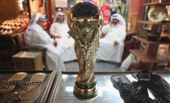 Arab men sit at a shoemaker's stall with a replica of the FIFA World Cup trophy in the Souq Waqif traditional market