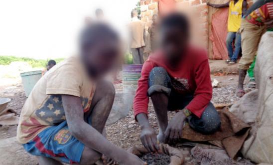 Two young children crouch and sort through rocks to find cobalt, a key metal used in the manufacture of car batteries