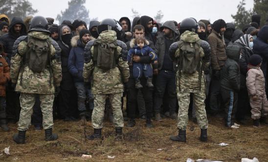 Migrants stand in front of Belarusian servicemen as they gather in a camp near the Belarusian-Polish border in the Grodno region on November 14 2021