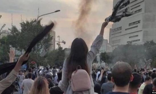 A person sits on someone's shoulders at a protest and waves a scarf