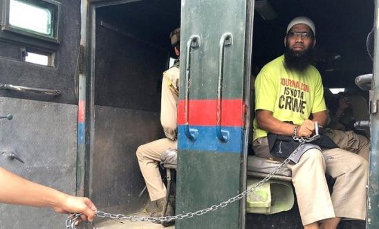 Picture of a man being held in chains in a military vehicle.