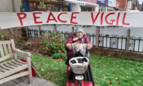 person on a mobility scooter in front of a peace banner