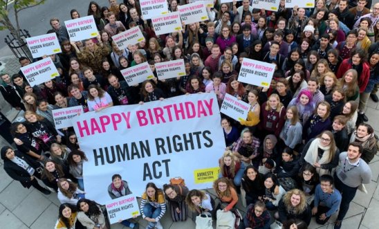 A group of few dozen people holding a banner saying Happy Birthday Human Rights Act