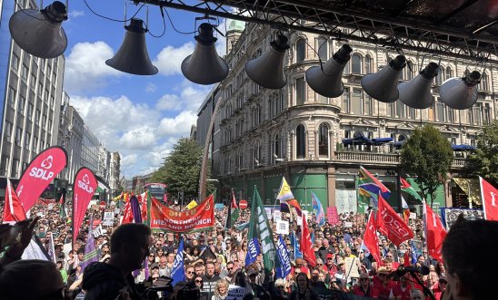 Colourful view from the stage of thousands of people - many holding aloft banners, flags and placards - gathered in front of Belfast City Hall to rally against racism.