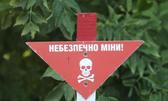 Sign in red and white with skull and crossbones and writing warning of mines ahead