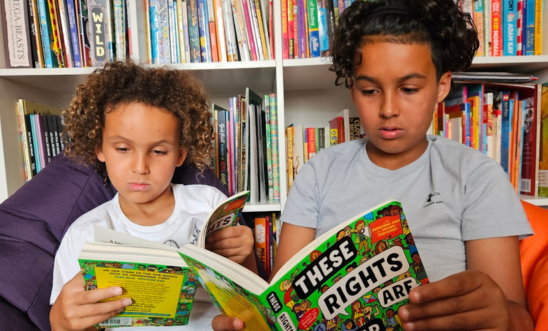 Image shows two children individually reading Amnesty's book "These Rights are Your Rights"