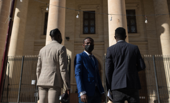 The El Hiblu three stand outside old building wearing suits on three-year anniversary of their rescue at sea